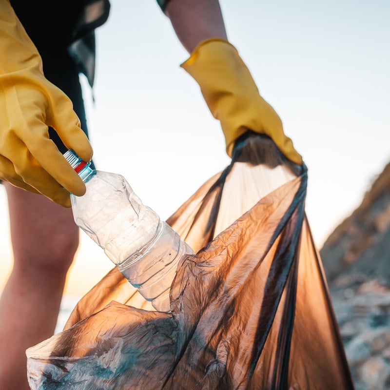 Person discarding plastic water bottle into a recycling bag.