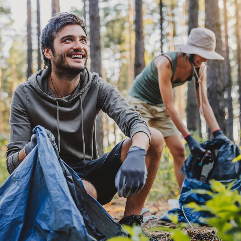 Two people working together to clean up trash in the woods.